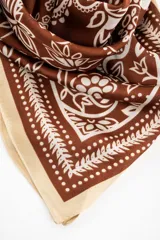 Bandana de diseño cuadrado en tono marrón y blanco con estampado de arabescos y flores, con bordes en color marfil.