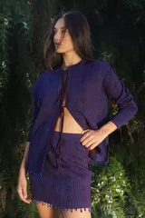 Cardigan de punto en color violeta con destellos de lurex, diseño de manga larga y cierre frontal con lazos. Presenta detalles de mostacillas en el ruedo.
