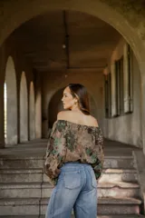 Blusa de lino con diseño off-shoulder, mangas largas amplias y estampado floral en tonos tierra y verdes.