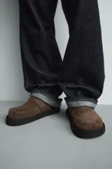 Zueco marrón de piel con acabado serraje, detalle de cinta en el empeine, plantilla acolchada, horma redonda y suela con volumen.