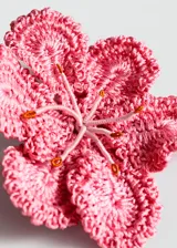 Broche en forma de flor de gran tamaño, confeccionado artesanalmente en tejido de crochet con hilo de poliéster en color rosado.