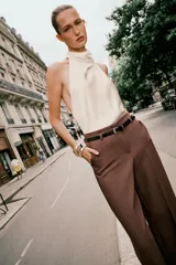 Pantalón de vestir color beige, tiro alto, corte ancho y pierna recta. Presenta un bajo con vuelta y viene acompañado de un cinturón fino de cuero marrón con hebilla metálica.