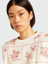 Remera sin mangas color crema con cuello redondo y estampado de flores, pájaros y frases en color rojo.