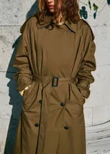 Trench coat largo oversize de color verde militar, con cierre de doble botonadura, trabillas en los hombros, cuello camisero de pana, cinturón con hebilla y trabillas ajustables en los puños.