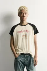 Camiseta regular fit de corte clásico con efecto lavado, cuello redondo negro y mangas cortas ranglán negras. El cuerpo es de color blanco con estampa frontal inspirada en automovilismo con el texto "Asphalt Speed".