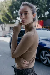 Jersey de punto liso en color beige, con cuello alto y manga larga con detalle de botones metálicos en los puños.
