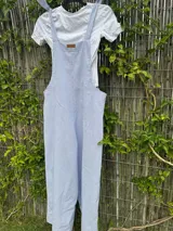 Mono largo de corte holgado con diseño de rayas verticales finas en azul y blanco. Presenta breteles anchos para atar sobre los hombros y piernas de corte ancho tipo palazzo.