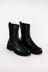 Bota tipo chelsea de cuero acharolado negro, con elásticos laterales y suela track dentada.
