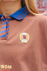 Remera tipo polo de manga larga con diseño de mangas raglán a rayas horizontales azules y blancas. El cuerpo de la prenda es blanco, con cuello polo y una pequeña estampa en el pecho. Confeccionada en tejido de algodón con spandex.