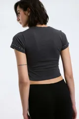 Remera blanca de algodón con cuello redondo y mangas cortas. Presenta pequeños apliques metálicos plateados alrededor del cuello y en las mangas.