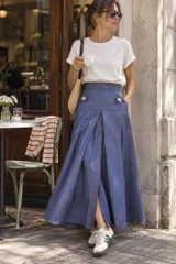 Falda larga de jean color azul con costuras en hilo rojo, cintura alta, bolsillos delanteros decorados con botones y cierre frontal abotonado con abertura central.
