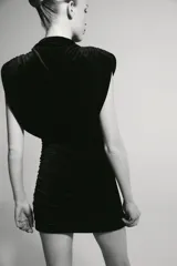 Vestido corto de cuello barco y diseño sin mangas con hombreras marcadas. Presenta un acabado satinado con detalle de frunces laterales y en la parte superior, aportando un efecto drapeado.