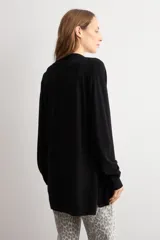 Ruana negra de tejido de punto, con mangas largas y cordón ajustable en la cintura.