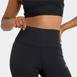 Calza deportiva New Balance de tiro alto, color negro liso, con pequeño logo reflectante en el muslo.