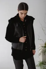 Chaleco de piel sintética en color chocolate, con cierre frontal y detalles de cuero en los bordes. Presenta un diseño de cuello solapa y ajuste lateral con hebillas.