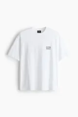 Remera blanca de punto de algodón, con cuello redondo y hombros caídos, corte holgado. Presenta un pequeño estampado en el pecho con el texto "MENTON FRANCE" en color oscuro.