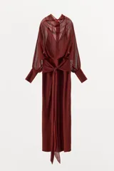 Vestido largo fluido en color bordó, confeccionado en georgette. Presenta cuello redondo, mangas largas con pliegues terminadas en puños y tiras ajustables para atar en la cintura. Incluye forro interior a tono.