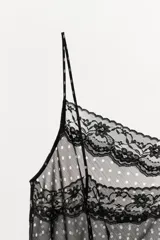 Top de tirantes finos con estampado de lunares, confeccionado en tejido semitransparente. Presenta detalles de encaje en el escote y un bajo asimétrico con volantes.