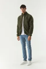 Campera de sherpa color verde militar, con cierre frontal completo, cuello alto y bolsillos laterales con cierre. Presenta un parche pequeño con logo en el pecho.