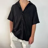 Camisa de manga corta con textura tejida, corte oversize y cuello solapa. Presenta cierre frontal con botones a tono.