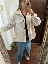 Campera de pana color blanco marfil, con bolsillos frontales con solapa, bolsillos laterales ojetes, cierre con botones oscuros y detalles de terminaciones deshilachadas.