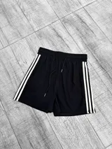 Short negro con cintura elástica y cordón ajustable. Presenta tres líneas verticales blancas en los laterales.