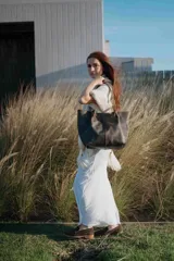Bolso tipo tote de cuero con acabado envejecido en tonos oscuros. Presenta doble asa de hombro con detalle de tachas metálicas y nudos decorativos en la unión con el cuerpo del bolso. Cuenta con un diseño amplio y estructurado.