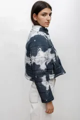 Campera puffer corta con cuello alto, cierre frontal con botones a presión y estampado abstracto de puntos en tonos azul oscuro y blanco.
