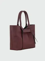 Bolso de hombro tipo tote bag de cuero color borgoña, con asas superiores y correa ajustable. Presenta un diseño estructurado con pliegues verticales y un detalle de borla colgante.