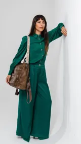 Mochila de símil cuero color marrón con apertura superior y tres bolsillos frontales con cierres metálicos. Cuenta con bolsillos laterales y una correa de galón con diseño geométrico, regulable y extraíble, que permite su uso como bandolera.