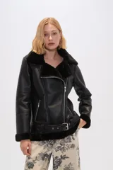 Chaqueta negra de cuero sintético con interior de piel sintética, corte al cuerpo, cierre frontal asimétrico con cremallera, cuello solapa con hebillas y cinturón con hebilla en la cintura.