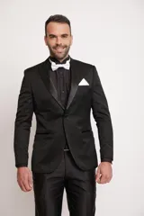 Ambo de corte slim fit compuesto por saco y pantalón. El saco presenta un tejido con sutiles patrones brillantes, solapas satinadas y bolsillos con ribete satinado. Se complementa con una camisa negra, moño blanco y pañuelo de bolsillo blanco.