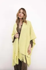 Ruana de tejido de punto color amarillo, con diseño abierto y terminación de flecos en el ruedo.