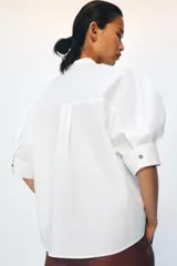 Camisa de popelín de algodón con cuello mao y cierre frontal asimétrico con botones a contraste. Presenta mangas cortas abullonadas y bajo recto.