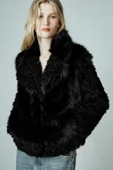 Abrigo corto de Zara Woman Collection con cuello de solapa y manga larga. Presenta una combinación de texturas con aplicación de pelo sintético y diseño de efecto rizado en mangas y bordes. Cuenta con forro interior y cierre frontal mediante ganchos metálicos.
