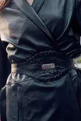 Tapado largo estilo trench de cuero ovino negro, con silueta recta, solapa amplia y cierre frontal cruzado ajustable con lazo en la cintura. Cuenta con bolsillos laterales funcionales y largo midi por debajo de la rodilla.