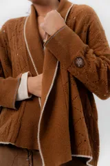 Saco tejido de lambswool color marrón, con diseño inspirado en kimono, mangas largas y delicados calados en toda la prenda. Cuenta con bordes en contraste.