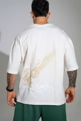 Remera oversize de algodón color off-white, con mangas cortas amplias y cuello redondo. Presenta un pequeño estampado en el centro del pecho y un diseño gráfico más grande en el lateral inferior.