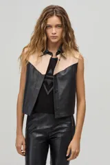 Chaleco de cuero negro y beige con cuello camisero, sin mangas y cierre frontal con botones a presión. Diseño con canesú en contraste y corte recto.