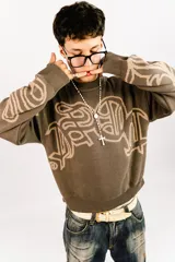 Sweater tejido reversible de corte boxy fit, con cuello redondo y puños acanalados. Presenta un diseño gráfico abstracto de estilo gótico que recorre el pecho y las mangas. Un lado es de color marrón oscuro con detalles en beige, y el otro lado es de color beige con detalles en marrón oscuro.