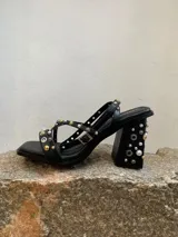Sandalias negras con tiras finas adornadas con apliques metálicos y perlas. Taco de 9 cm y base cuadrada.
