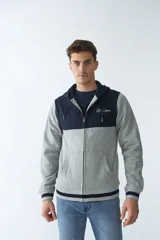 Campera de felpa gris con capucha y cordón ajustable, cierre frontal con cremallera, bolsillos laterales, mangas largas y logo estampado en el pecho.
