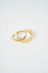 Set de dos brazaletes dorados de metal. Uno es liso y ancho, con textura martillada. El otro es más fino, con borde irregular.