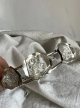 Gargantilla plateada con tres dijes de metal con forma de flor y relleno de piedras blancas.