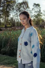 Cardigan de lana color celeste con cuello redondo, cierre frontal con botones color naranja y flores bordadas en azul y celeste.