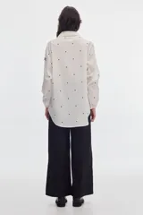 Camisa oversize blanca con estampa de lunares negros, cuello en pico con solapas clásicas y mangas abullonadas con puños elásticos.