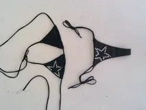 Bikini de dos piezas color blanco, con corpiño triangular decorado con tachas hotfix en forma de estrella y bombacha a juego con textura brillante.