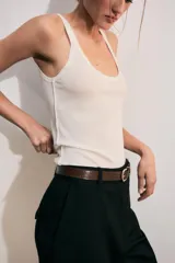 Pantalón de tiro alto color negro, de corte recto y pinzas frontales. Incluye un cinturón delgado de cuero marrón con hebilla metálica dorada.
