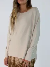 Sweater de punto color beige con sutiles destellos brillantes, cuello redondo, manga larga y diseño con ruedo asimétrico más largo en la parte trasera.