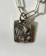 Collar de plata con cadena de eslabones tipo clip y dije rectangular texturizado con detalles en relieve y piedras verdes incrustadas.